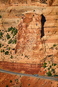 岩石的垂直长高红色大墙 道路狭小 汽车切割横穿图片