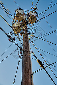 上面有三桶木制电话杆 顶上有许多在晴蓝天空上的汇合电话线图片