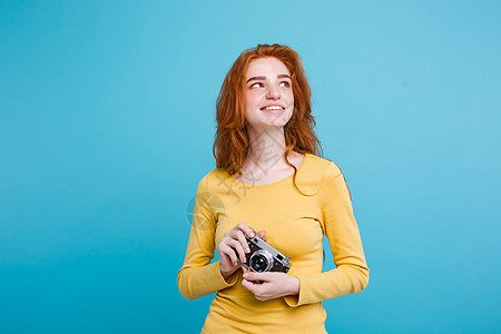 旅行概念  特写Portrait年轻漂亮的红头发女孩Wtih时尚帽子 太阳镜和古老的相机 微笑在镜头前笑 蓝面纸背景 复制空间季图片