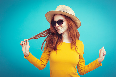 旅行概念     特写肖像 年轻漂亮的有吸引力的红头发女孩Wtih时尚帽子和墨镜笑脸 蓝面纸背景季节衣服魅力海滩女士太阳镜微笑假图片
