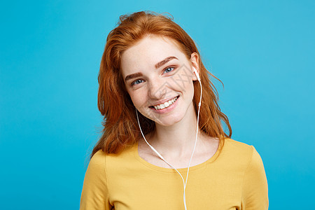 生活方式概念  快乐的姜红发女孩的肖像享受听音乐 耳机微笑地笑着对镜头 在蓝面画背景上被孤立 复制空间播放技术收音机手机工具歌曲图片