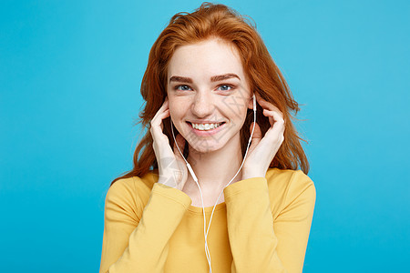 生活方式概念  快乐的姜红发女孩的肖像享受听音乐 耳机微笑地笑着对镜头 在蓝面画背景上被孤立 复制空间技术唱歌黄色旋律列表歌曲舞图片