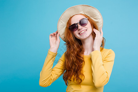 旅行概念     特写肖像 年轻漂亮的有吸引力的红头发女孩Wtih时尚帽子和墨镜笑脸 蓝面纸背景蓝色季节太阳镜海滩魅力太阳裙子女图片