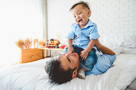 两个亚裔父亲和他的儿子躺在卧室的床上玩耍 孩子高兴地趴在日本爸爸身上 空闲时间 人们生活方式健康情感爱 检疫 Covid-19 图片