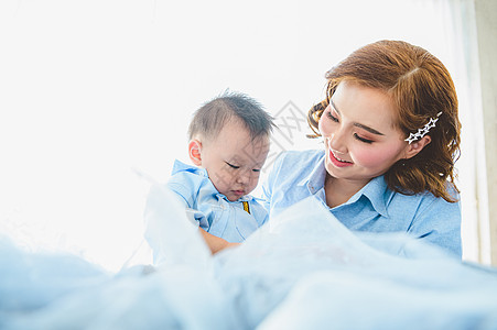亚洲母亲和她的儿子在卧室的床上穿着蓝色衬衫 家里有复印空间 人们的生活方式和新生儿医学概念 Covid-19 或冠状病毒流行病主图片