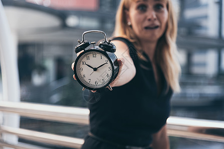 商界女性在城市背景下上班时 会显示闹钟 并对晚高峰时间感到震惊 截止日期和起床晚 人们的生活方式和日常生活规划师的概念压力女士小背景图片