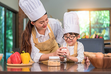 亚洲妈妈穿着厨师制服帮助可爱的小男孩在家里的厨房里喝玻璃杯牛奶 人们的生活方式和幸福的家庭团聚理念 牛奶营养中的钙和蛋白质图片