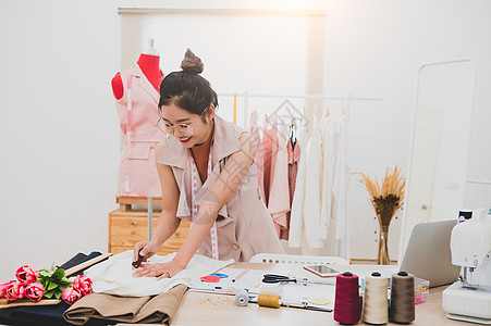 在家庭办公室车间工作的迷人亚洲女性时装设计师 时尚的时尚达人女性创造新的布料设计系列 裁缝和缝纫 人们的生活方式和职业概念手工店图片