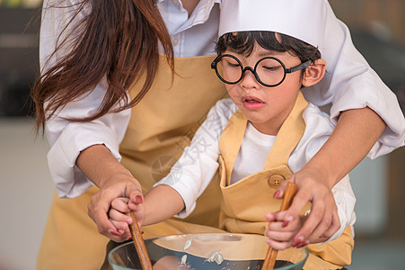 戴着眼镜的快乐可爱小男孩和美丽的亚洲妈妈准备在家里的厨房里做饭 人们的生活方式和家庭 自制食品和配料的概念 两个泰国人的生活图片