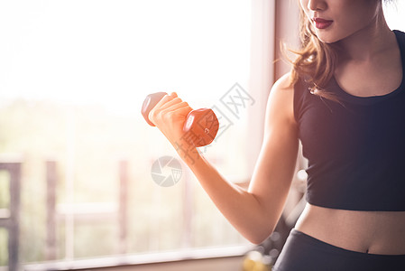 运动女子的手举起哑铃 用右手在窗户附近进行重量训练 以抽取二头肌 锻炼和身体建立概念 室内健身馆和医疗保健主题图片