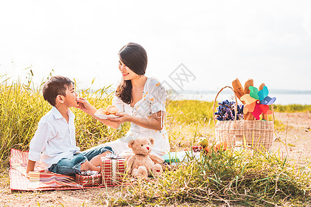 美丽的亚洲妈妈在野餐时在草地上给儿子喂零食 母亲和儿子一起玩耍 在母亲节庆祝和欣赏概念 夏天的人和生活方式的主题图片