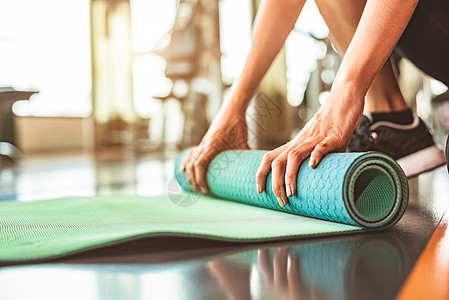 在运动健身健身房训练中心背景下特写运动型女性折叠瑜伽床垫 瑜伽课后保持运动垫滚动 锻炼和运动训练概念 手放在地毯上活动活力赤脚女图片