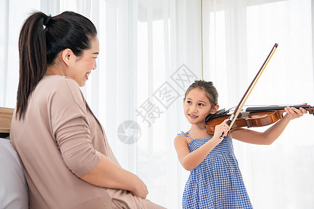 女孩与怀孕母亲一起为婴儿腹部的新生儿玩小提琴 音乐和娱乐概念 (笑声)图片