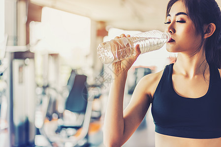 亚洲女性在有健身器材背景的健身馆锻炼或运动训练后饮用纯净饮用水以保持新鲜 放松和休息的概念 力量和健身训练主题图片