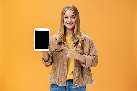 准备迎接秋天的半兽人 配上新的数字平板电脑 穿着电线内衣的迷人女性肖像显示小工具屏幕指向装置 在橙色墙面上微笑欢乐和友好青年销售图片