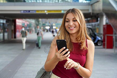 迷人的美丽商业妇女 利用智能手机在火车或地铁站行走 以随意方式微笑图片