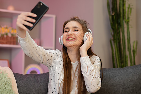 美丽的女人在家里听音乐 漂亮的微笑女孩在智能手机上自拍 听音乐 坐在家里的沙发上图片
