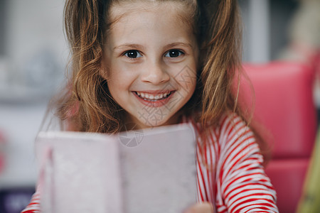 一个学龄前女孩看着镜头微笑的画像 小女孩坐在家里儿童房的办公桌前 在线学习 远程学习 在线学校家庭作业家庭生活技术男生写作小学生图片