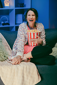 女孩在家里面对看喜剧电影 坐在沙发上看电视的千禧一代女性 娱乐的概念 积极的情绪图片