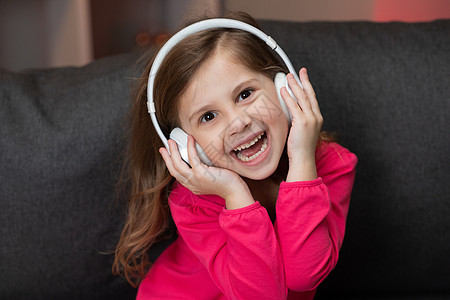 美丽可爱快乐的小女孩在无线耳机上听音乐 有趣的小女孩随着节奏跳舞 唱歌和移动 孩子戴着耳机图片