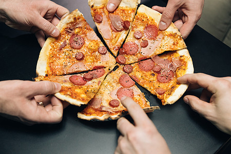 男性的手从送餐中取出披萨片 奶酪 西红柿和火腿 一群饥饿的朋友坐在办公桌前 在餐桌背景上分享美味的午餐手臂盘子食物闲暇送货烹饪派图片