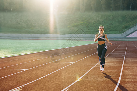 在体育场运动跑道上做有氧运动的黑色运动服跑步白人女性的前视图 成年女运动员慢跑 马拉松比赛前训练 健康 女运动员图片
