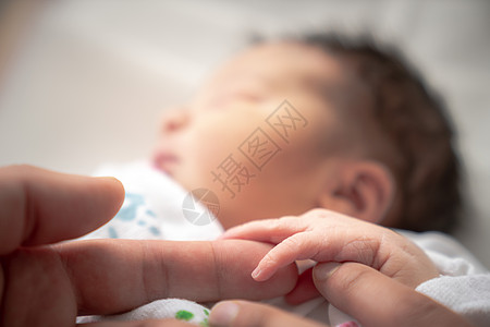 牵小手一个裹在襁褓中的新生女婴在安静地睡觉时 用她的小手和手指环绕着父亲和母亲的手指爸爸种族女儿孩子后代毯子婴儿混血棕榈家庭背景