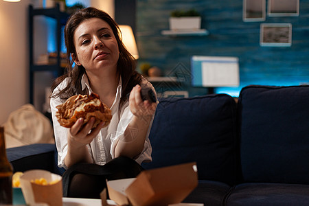 白种女性用远程看喜剧系列来改变频道 将美味的汉堡包握在手中图片