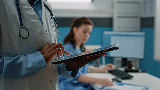 使用触摸屏的平板电脑 近距离接近非洲美洲医生保健药片工具卫生办公室诊断成人工作医师工人图片