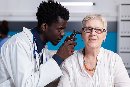 黑人青年医生对老年病人使用眼透镜男人耳镜长老测量金属咨询耳鼻喉科医院疾病工作图片