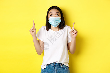 Covid19 大流行病和社会不协调概念年轻女性穿白色T恤衫和用医疗面具从科罗纳病毒中取笑并举起手指 显示特别报价隔离成人快乐情图片