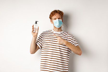 Covid19 健康和生活方式概念 笑得开心的红头男子面部面具用手指着洗涤剂 建议采用抗食药 白背景男性红色广告促销购物商业白色图片