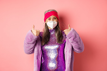Covid19 大流行病和时尚概念 在科罗纳病毒期间与呼吸器共患冠状病毒的亚洲高级女性愉快地聚会 举起拇指 建议佩戴面罩 粉红色图片