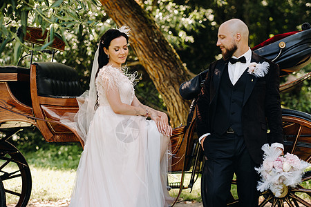 新娘和新郎中的一对夫妇正站在马车旁边 自然界中以复古风格女士花束已婚花朵领结夫妻裙子面纱新婚婚姻图片