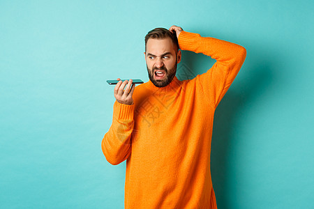 男人在用扬声器说话时抓头的疑心男子 用不果断的脸脸记录语音信息 穿着橙色毛衣站在浅蓝背景上购物手势潮人横幅广告快乐标识情感男性促图片