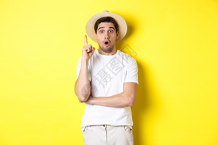 穿着草帽的年轻男子的肖像有想法 举起手指乌瑞卡标志 提出建议 站在黄色背景之上男性游客手势成人假期商业帽子广告促销情绪图片