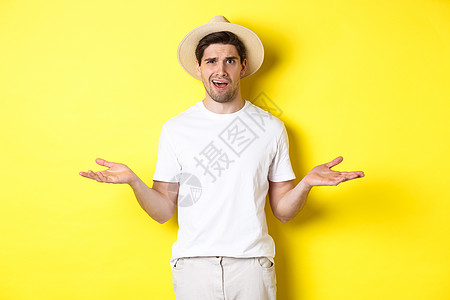 旅游和夏天的概念 迷糊的家伙旅行者挥舞 无法理解什么 站在黄色背景下站立着手势男性工作室微笑促销成人游客广告商业技术图片