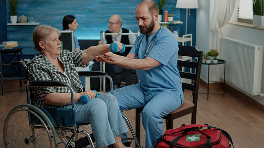 医疗助理帮助残疾妇女进行体育锻炼治疗保健病人活动安慰护士轮椅老年哑铃练习图片