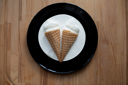圆形白色甜点甜美可口的冰淇淋蛋糕 在木板背景的黑色盘子上的华夫饼杯中装饰着两个冰淇淋甜筒 顶视图 特写早餐饮食饮料巧克力蛋糕美食图片