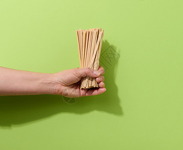 女性手持可支配木棍 用于在绿色背景下搅拌热饮 咖啡和茶匙图片