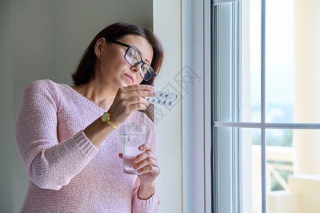 在家中手握着避孕药和水杯的中年妇女女性窗户治疗疾病药剂女士药片成人疼痛抗生素图片