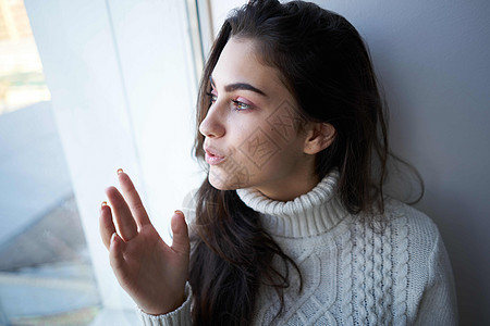 在窗户旁边穿着白毛衣的黑发女性成人孤独伤害疼痛女孩情感沮丧头发头痛图片