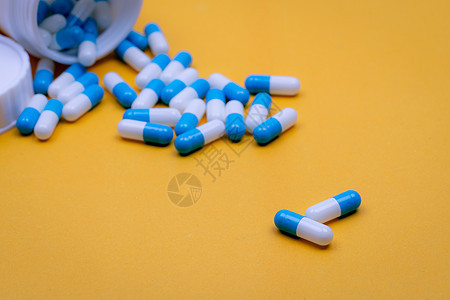 两个蓝白色的胶囊药丸模糊了许多从塑料药瓶中倒出的药丸 在黄色背景上的胶囊药丸 处方药 医药行业 保健和医学概念图片