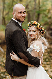 夫妻新娘和新郎在秋林中行走夹克花圈裙子婚礼树叶森林红色白色头发女孩背景