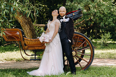 新娘和新郎中的一对夫妇正站在马车旁边 自然界中以复古风格新婚婚纱花束戏服女士已婚花朵大车运输套装图片