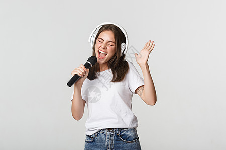 无忧无虑的笑笑女孩在唱卡拉OK 用麦克风和耳机唱歌情绪学生女士手势卡拉ok女性成人歌手女朋友快乐图片
