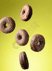 带多色糖的巧克力圆甜甜甜圈 在绿色背景上喷洒浮地蛋糕棕色装饰圆圈糕点甜点圆形磨砂面团工作室图片