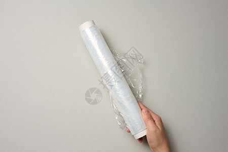两只女性手握着一卷透明的胶片 用于包装产品 灰色背景图片