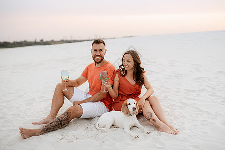 身着橙色衣服和狗的年轻夫妇夫妻裙子海滩蓝色沙漠白色海岸短裤橙子图片