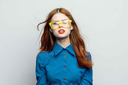 妇女穿着蓝色衬衫的黄色眼镜护目镜工作室金发女郎微笑魅力商业桌子衣服女士灰色女性图片